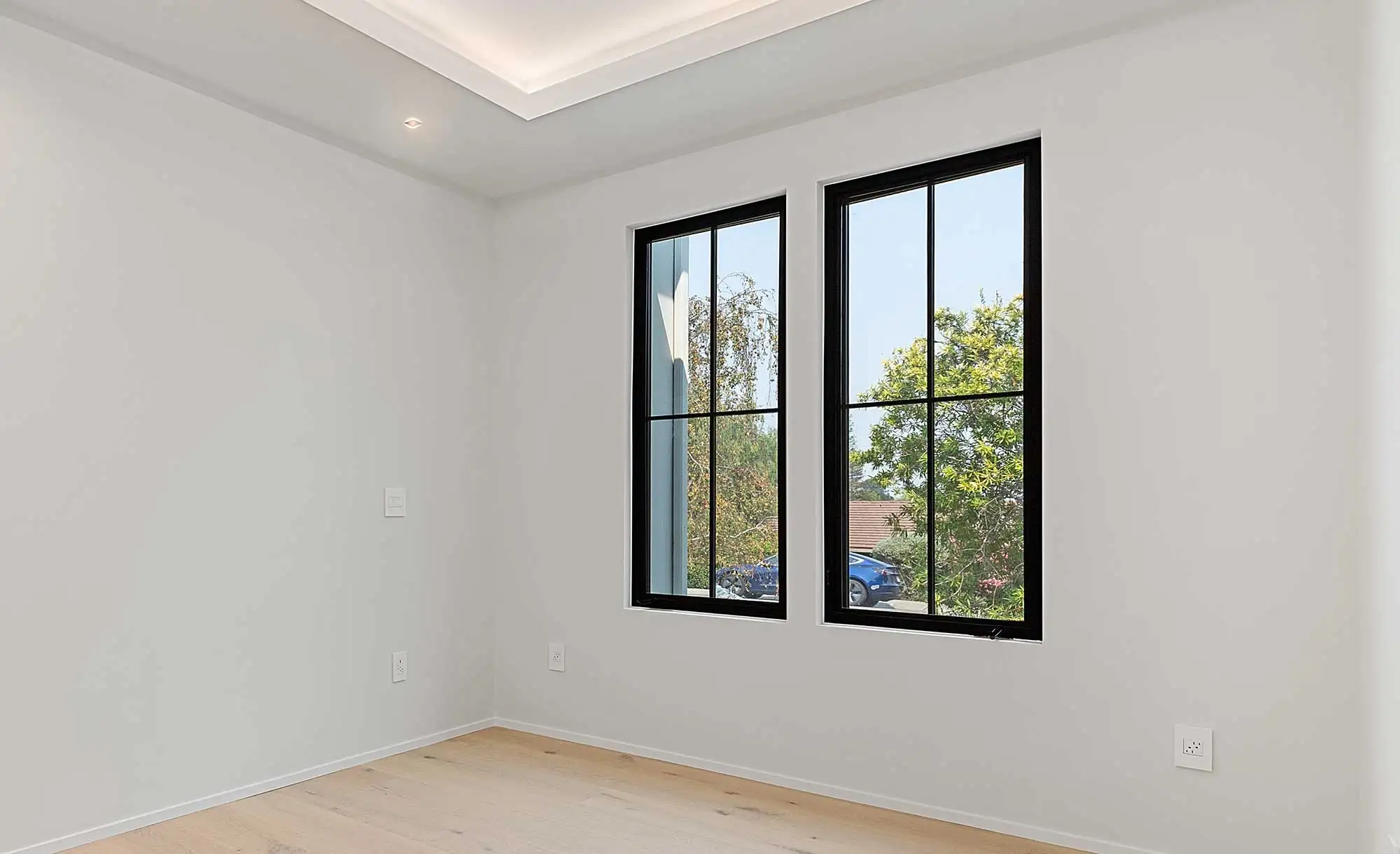 Modern interior room featuring energy-efficient black framed casement windows with grilles, light wood flooring, and recessed ceiling lighting for residential window installation.