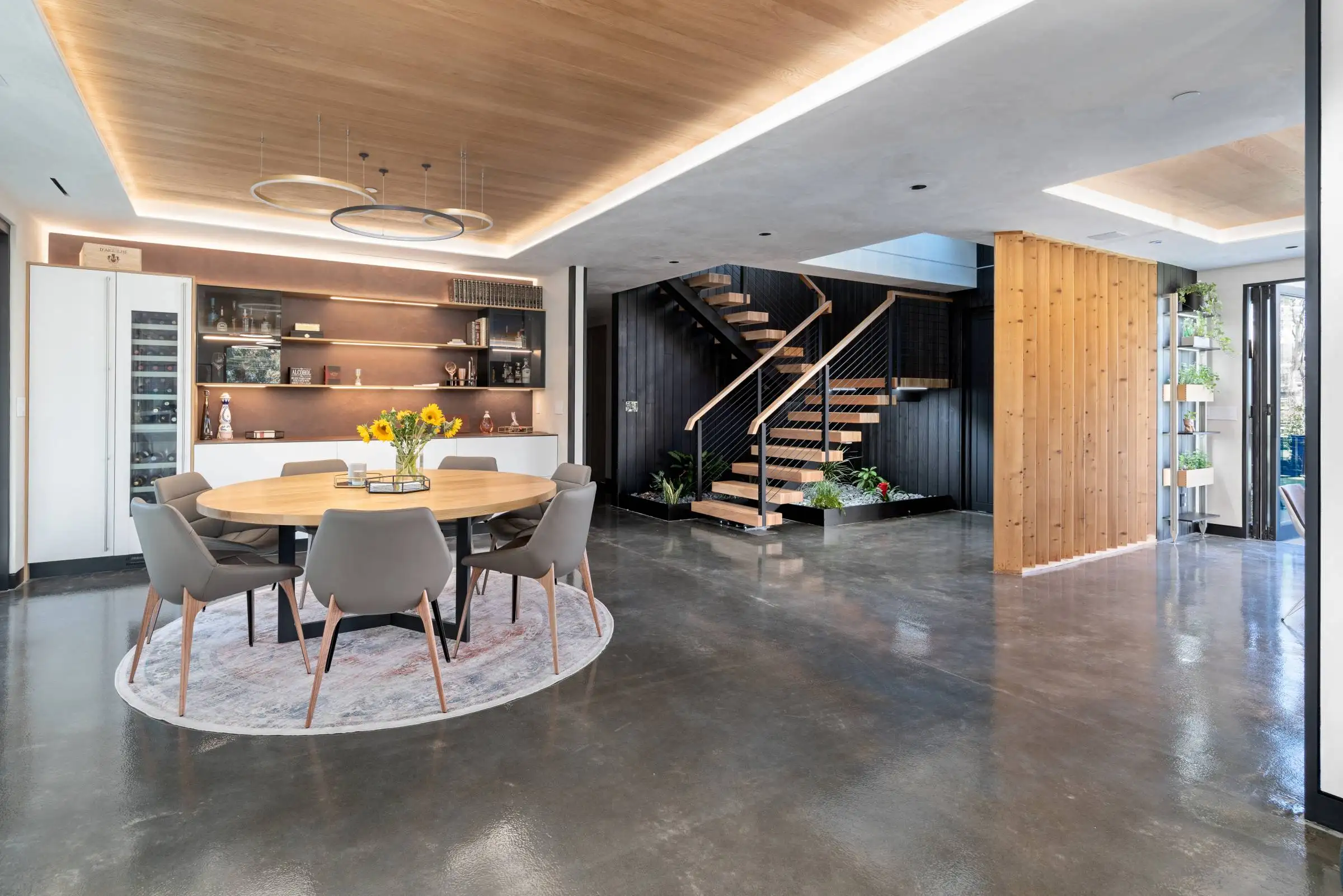 Luxury custom home interior featuring an open-concept dining room, polished concrete floors, custom floating staircase, and modern architectural design.