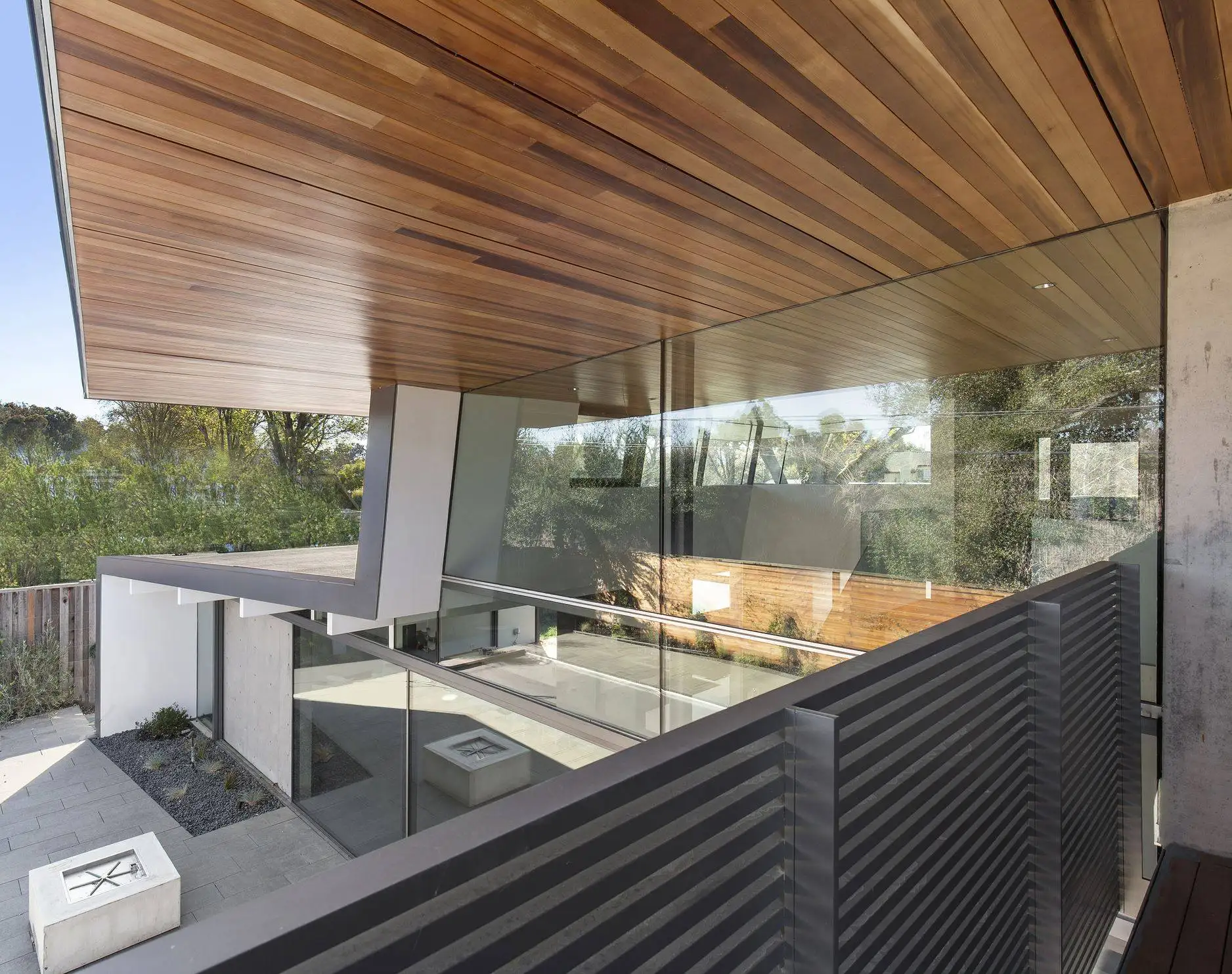 Close-up of a cantilevered wood ceiling overhang and glass railing on a modern home, framed by trees