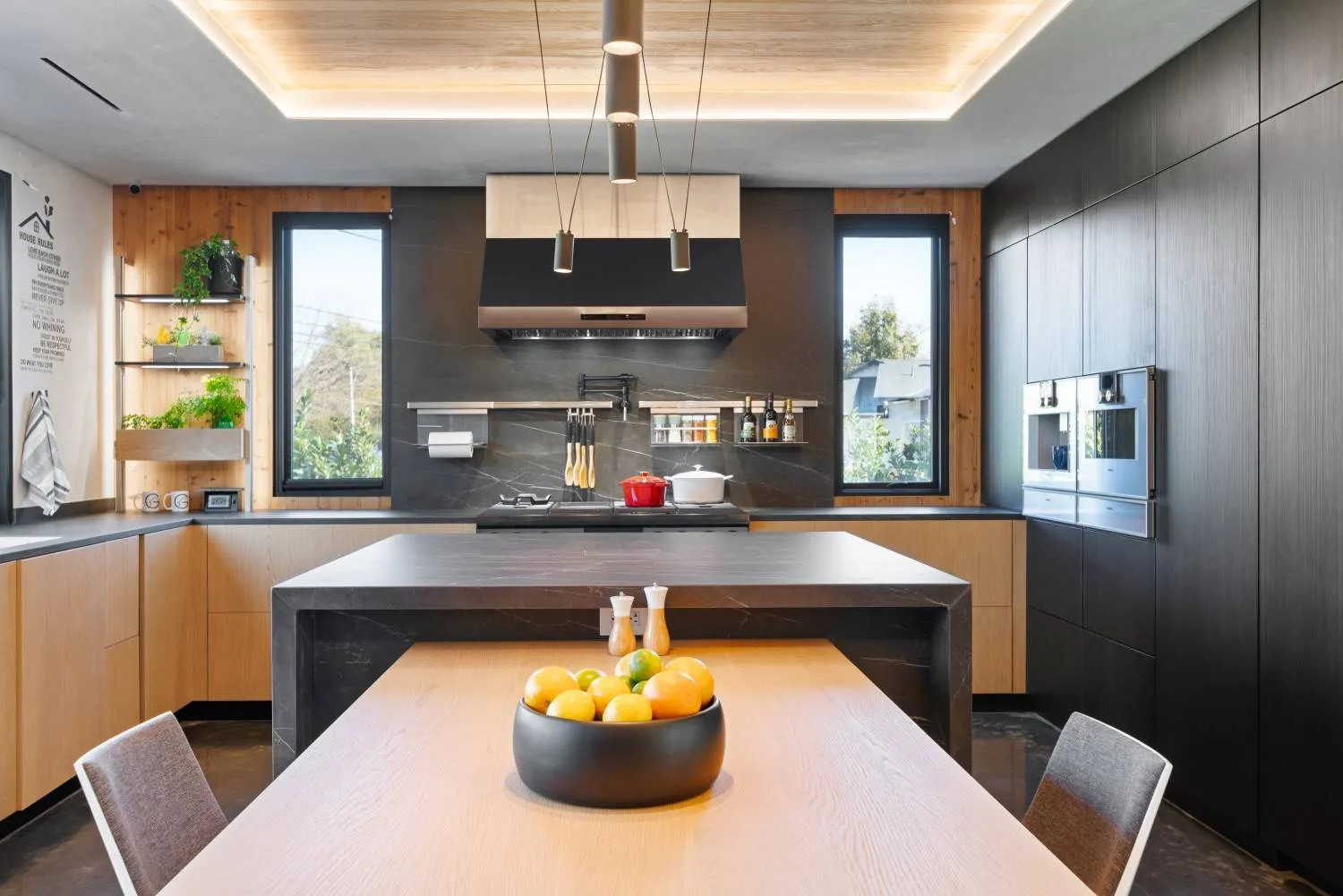 Luxury modern kitchen remodel featuring black waterfall island countertops, natural wood cabinetry, integrated appliances, and cove ceiling lighting.