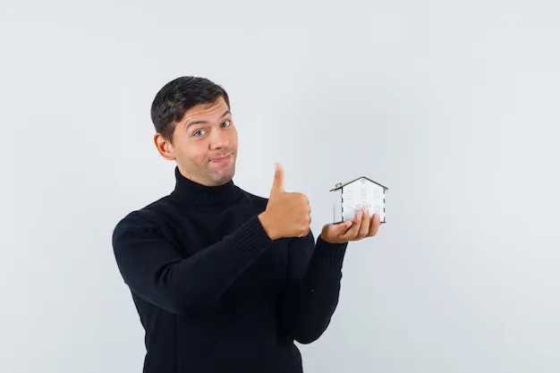 Homeowner giving a thumbs up while holding a small house model, symbolizing confidence in renovating rather than moving