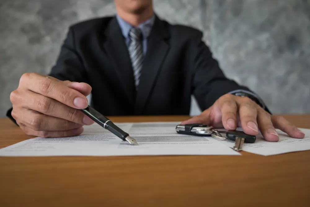 Professional in a business suit reviewing building permit documents and contract paperwork with a pen and set of keys on a desk.