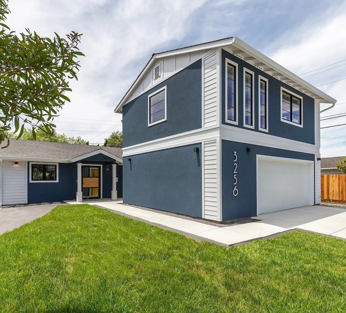 Two-story home exterior with navy blue stucco siding, white trim, and an attached two-car garage — representing a Bay Area remodel or rebuild project