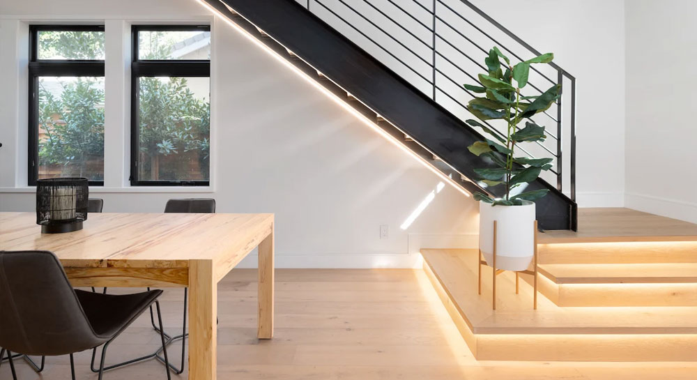 Modern staircase with LED strip lighting, black metal railing, and built-in wood steps, next to a dining area with a live-edge wood table