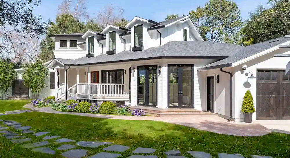 Single-story farmhouse-style home exterior with a covered front porch, dormer windows, black-framed French doors, and a landscaped front yard