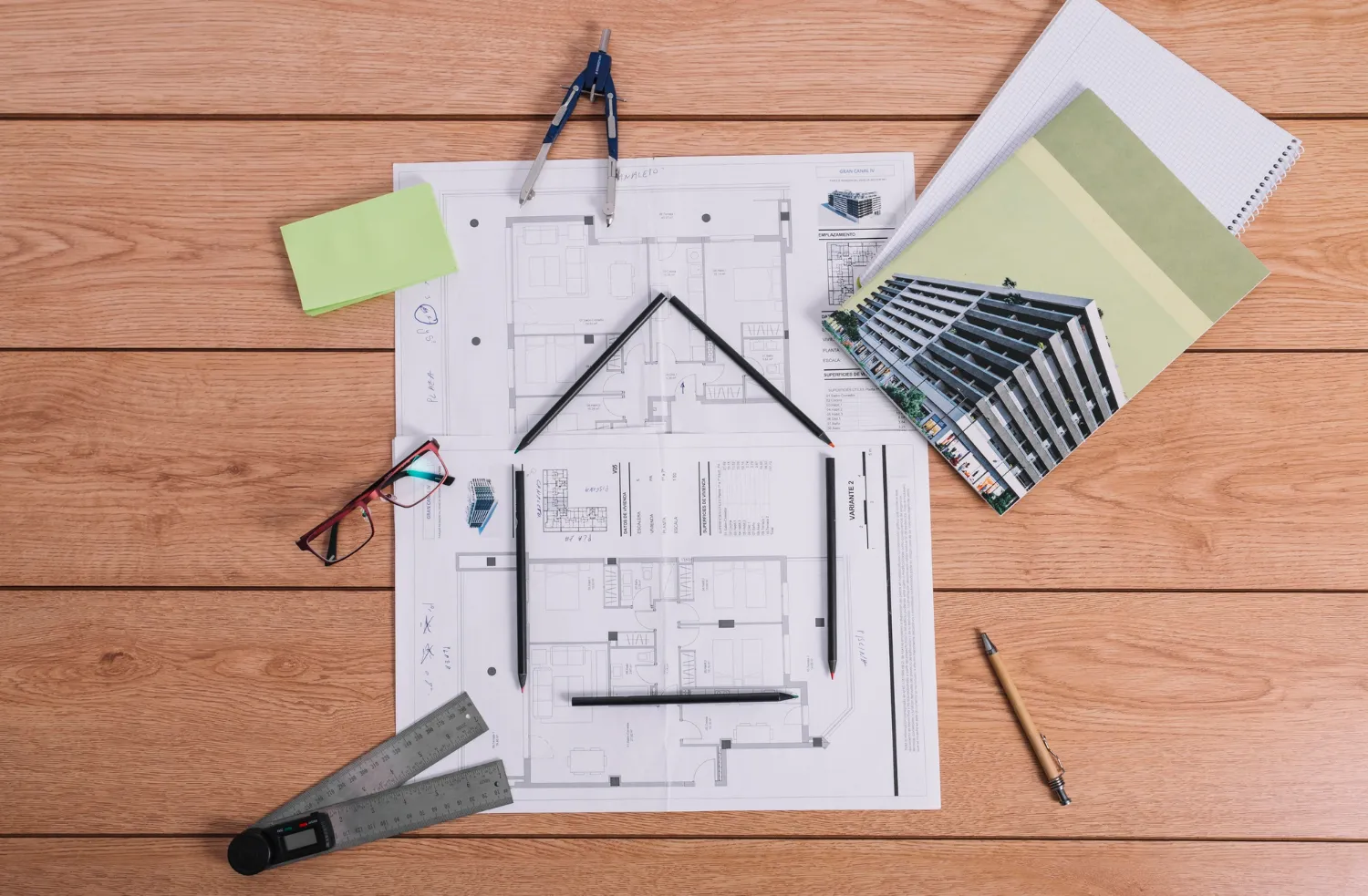 Architectural blueprints and drafting tools arranged on a wooden desk comparing modular and traditional residential construction design planning.