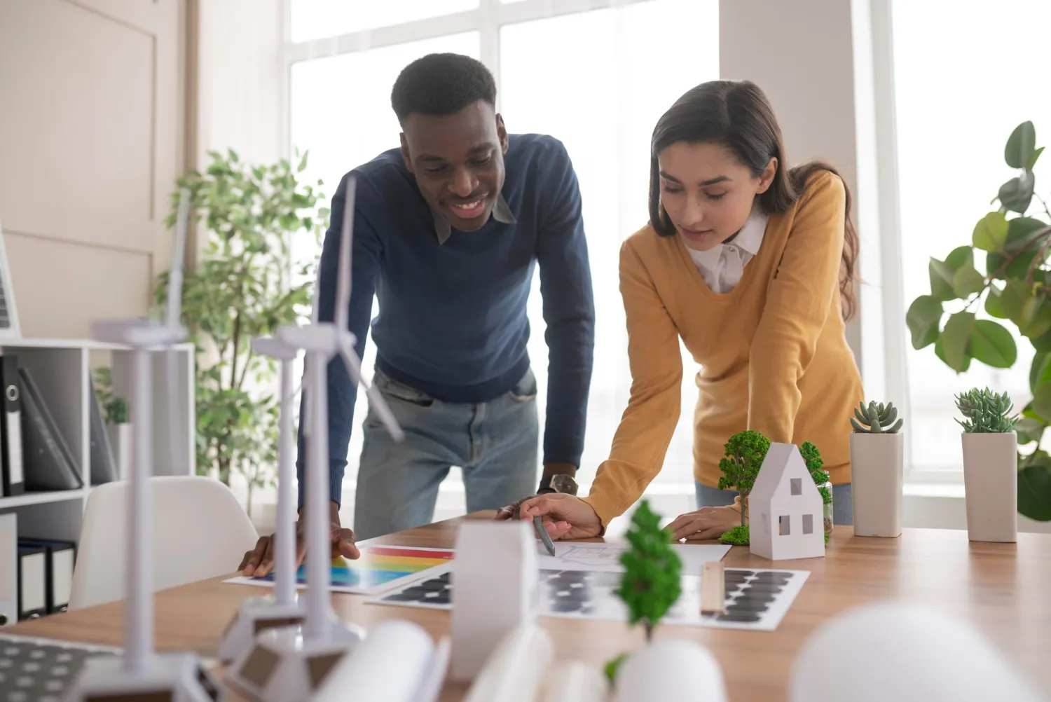 Architects planning sustainable home improvements in the Bay Area using eco-friendly architectural models, wind turbines, and solar panel designs.