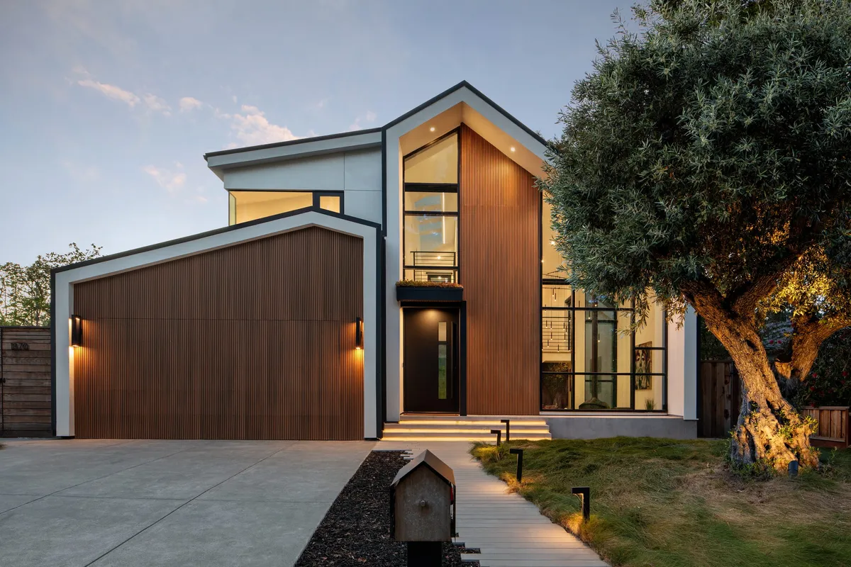 Modern Greenberg home with a timber-clad garage and paved driveway at dusk