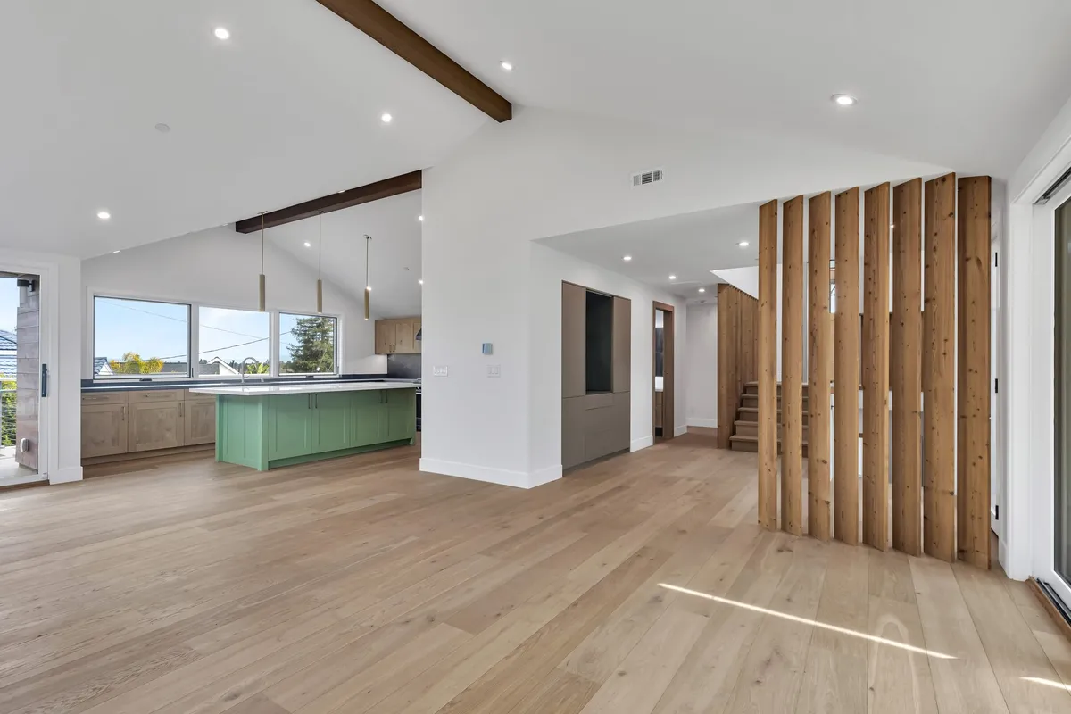 Open-plan living space with wood flooring, slatted screen, and sage-green kitchen island in a Greenberg Redwood City remodel