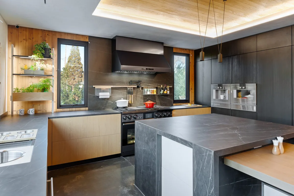 Kitchen with stone island, dark cabinetry, and wood finishes in Greenberg’s Colorado Ave new-build project in Palo Alto