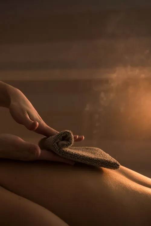 Hands holding a folded towel over a person's back with warm steam in soft lighting.