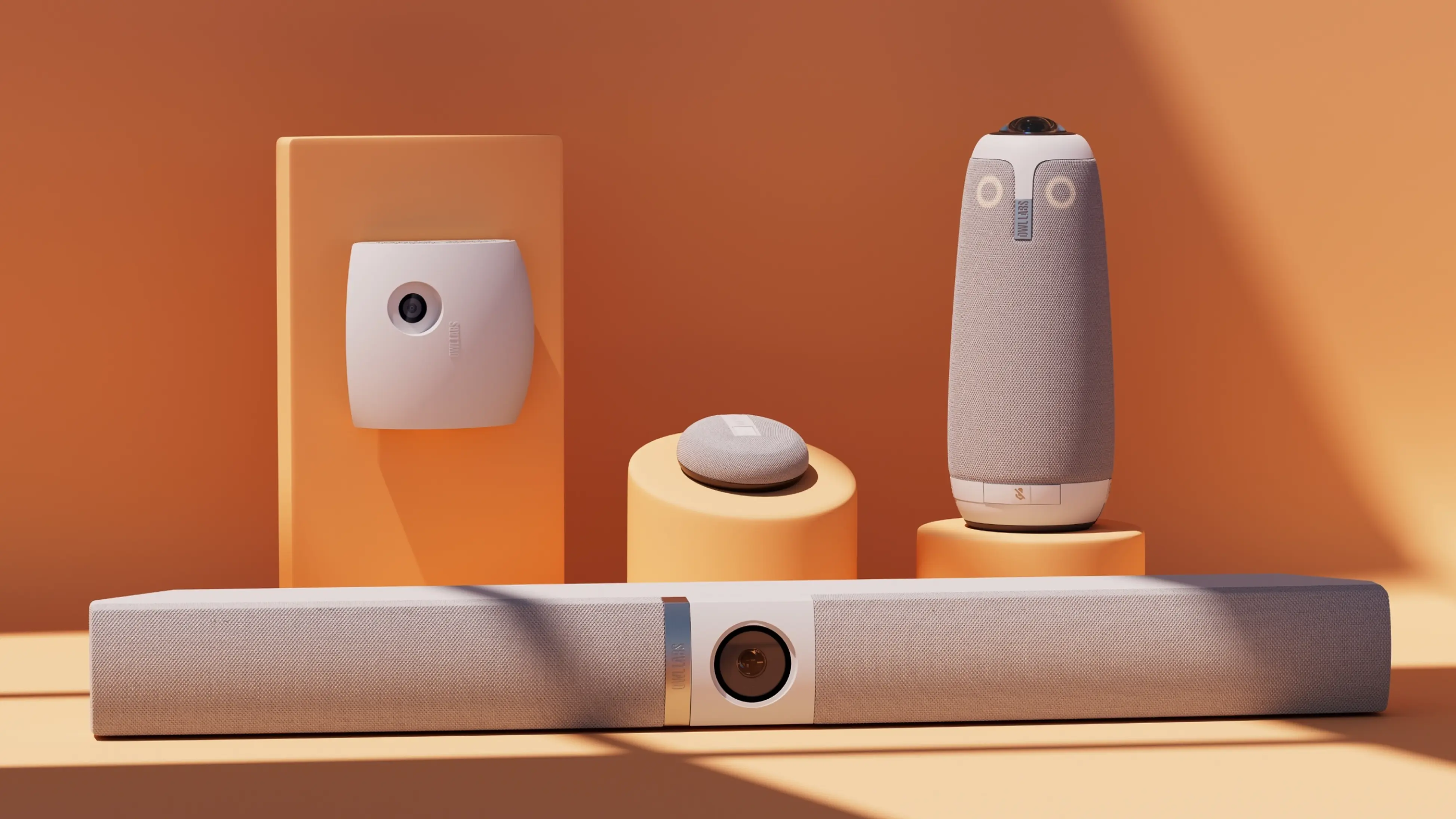 Four Owl Labs video conferencing devices in beige and white on orange pedestals and background: a wall-mounted camera, a small round speaker device, a tall cylindrical speaker with camera on top, and a long soundbar with a central camera lens.
