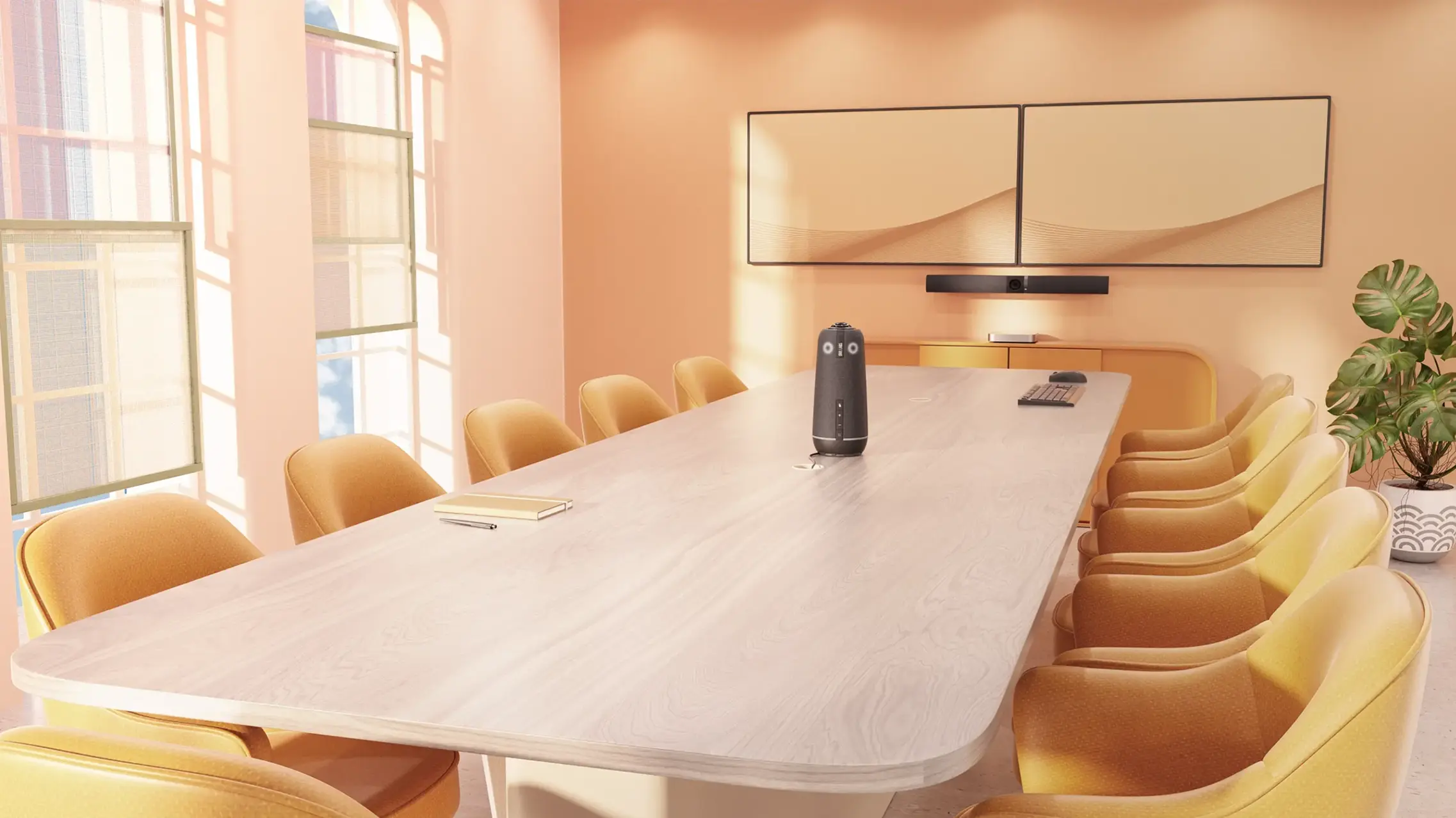 Bright conference room with a long light wood table surrounded by mustard-yellow cushioned chairs, two wall-mounted rectangular screens showing a minimal wave design, a conference speakerphone device in the center of the table, a notebook and pen on one side, a wireless keyboard and mouse on the other, and a potted plant in the corner near peach-colored walls with tall windows letting in sunlight.