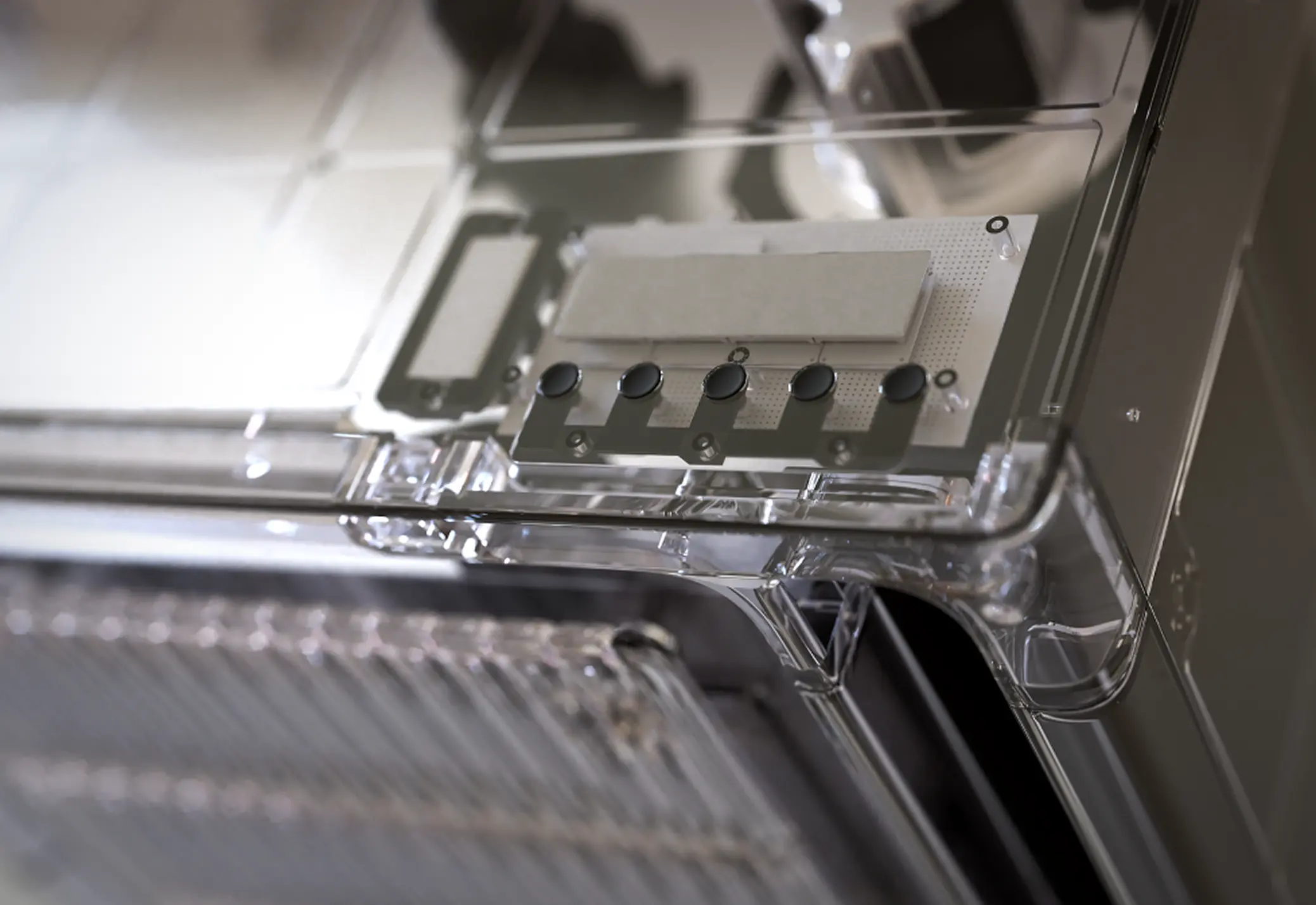 Close-up of a transparent casing containing a circuit board with five black circular components and a rectangular white chip.