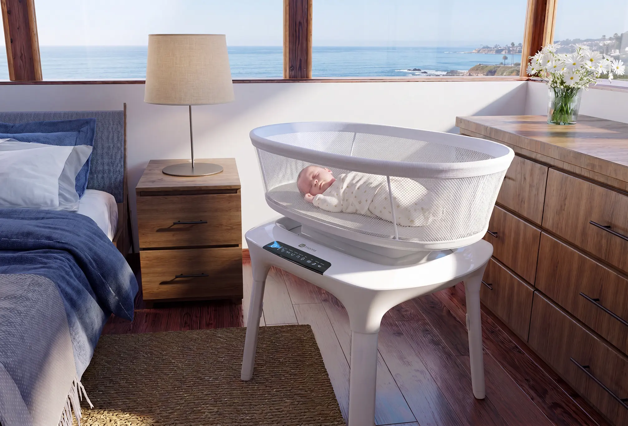 A baby sleeping peacefully in a modern white mesh bassinet placed on a white stand in a bedroom with wooden furniture, a lamp, and a view of the ocean through large windows.