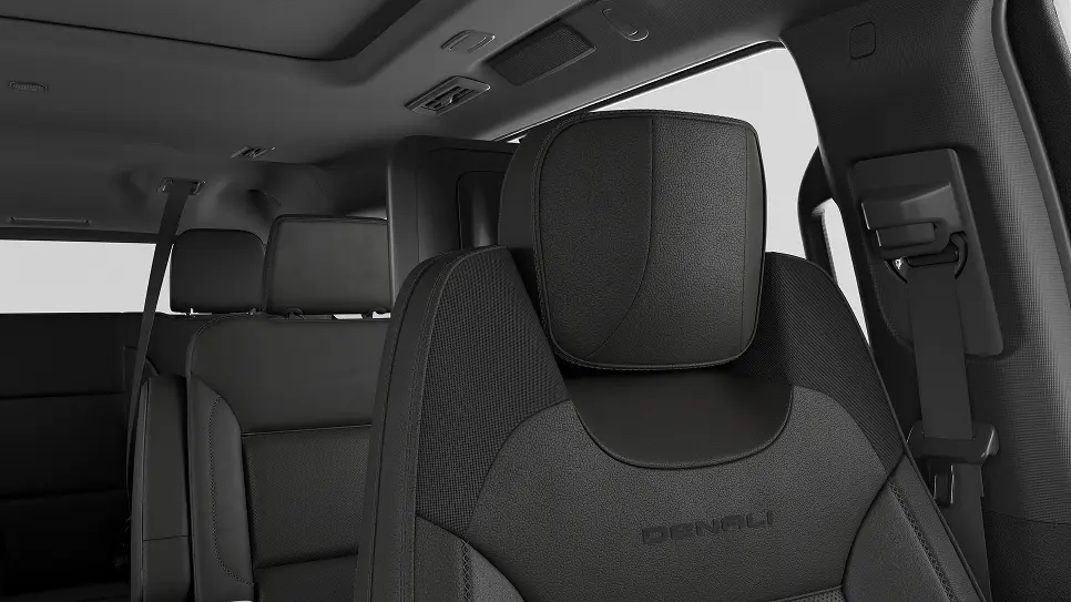 Close-up view of a black Denali car seat with a textured headrest inside a vehicle, showing part of the rear seats and a seatbelt on the right side.