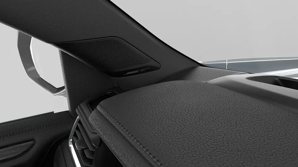 Close-up view of a car's interior showing the left A-pillar with a Bose speaker integrated, part of the dashboard, air vent, and the side mirror visible through the window.