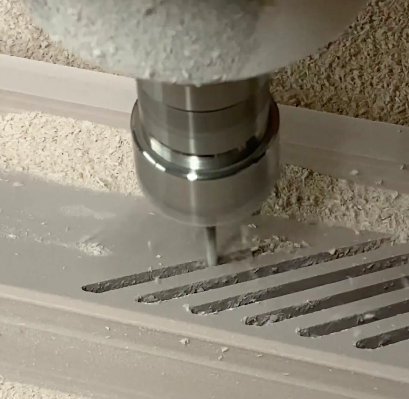 Close-up of a CNC milling machine cutting parallel slots into a light-colored material, producing fine dust around the engraved lines.