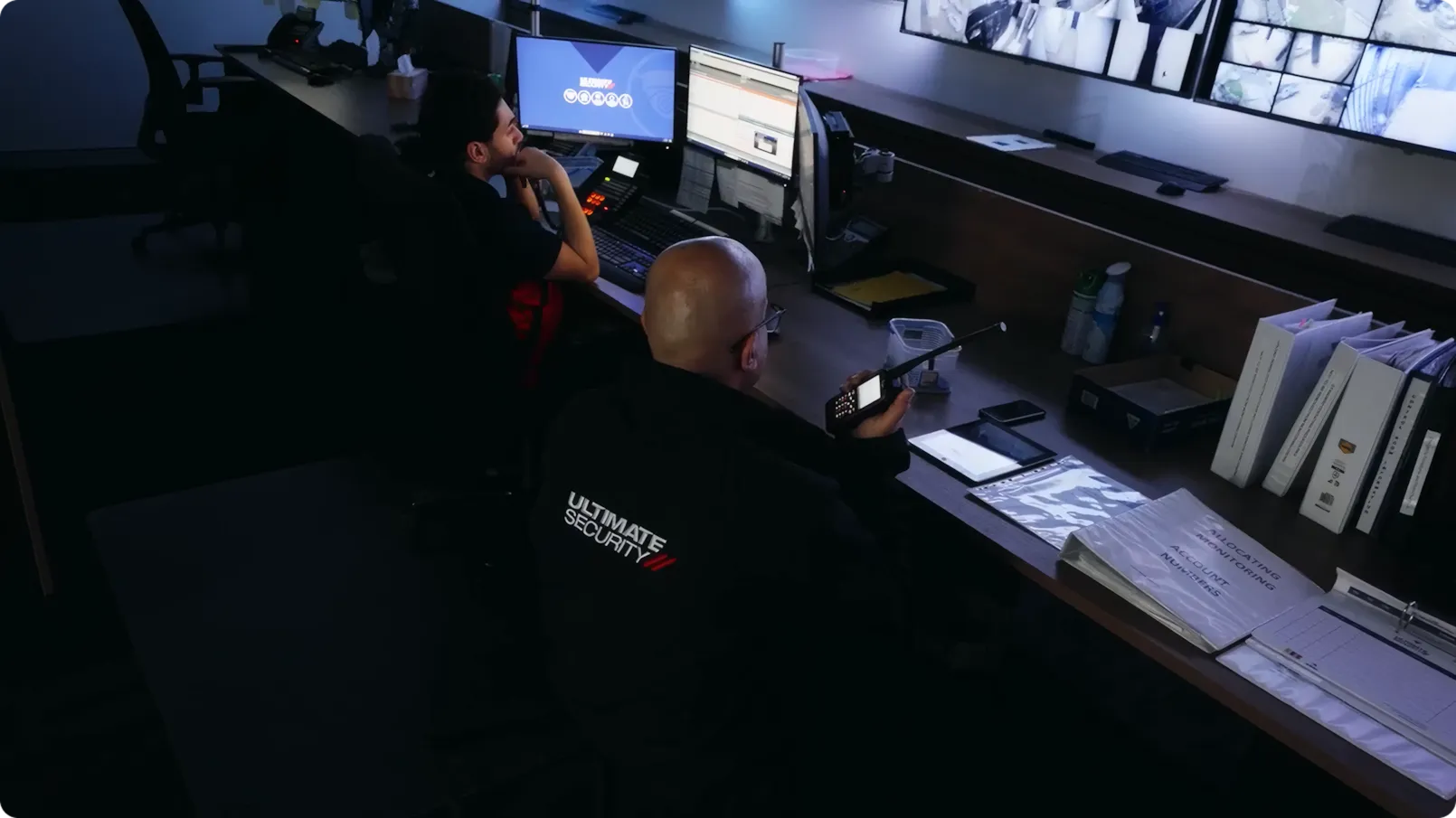 Ultimate Security team monitoring CCTV feeds from the security center while holding a walkie-talkie for communication