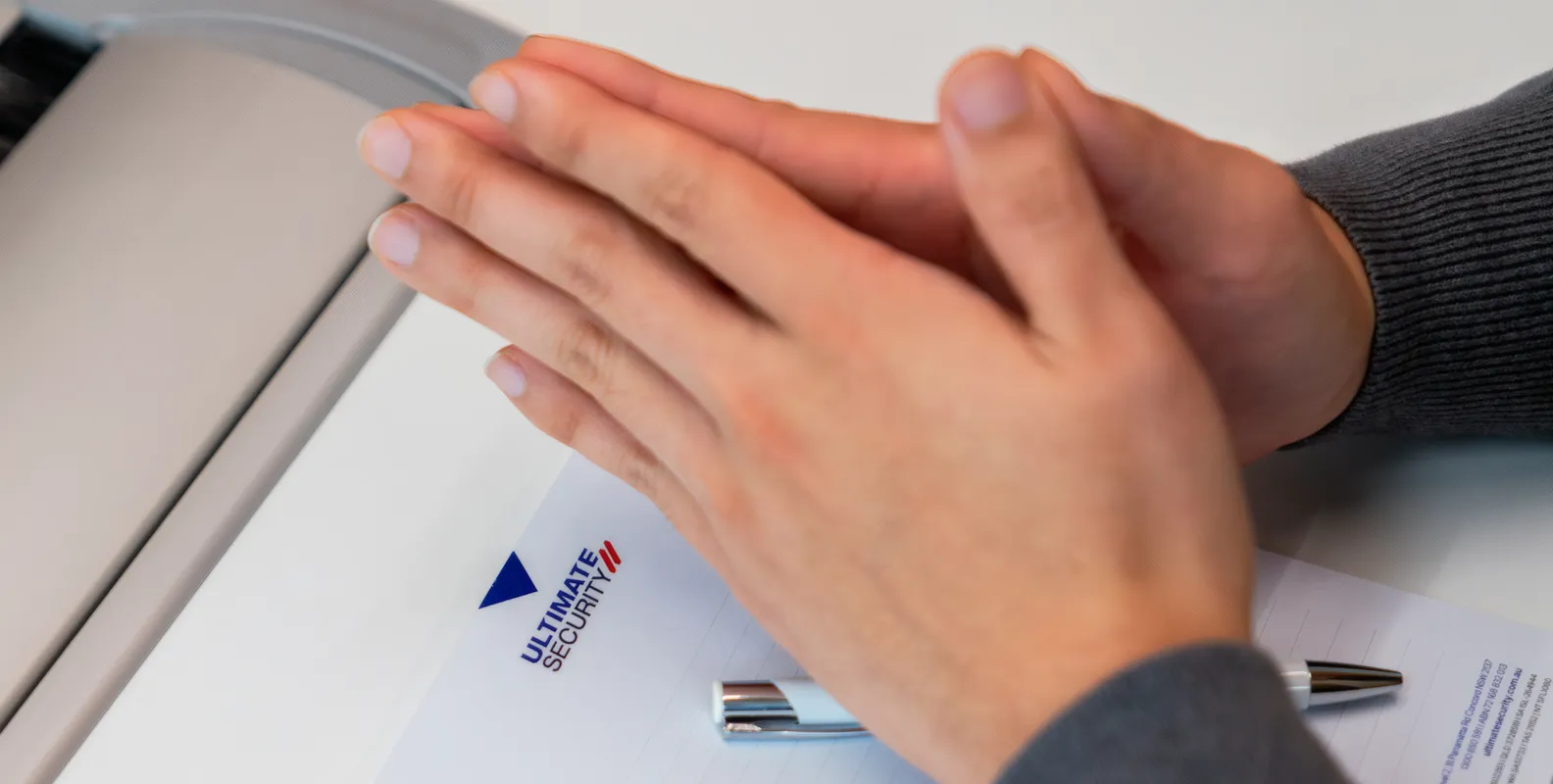 Close-up of a hand writing on paper with a pen, featuring the Ultimate Security logo for contact inquiries.