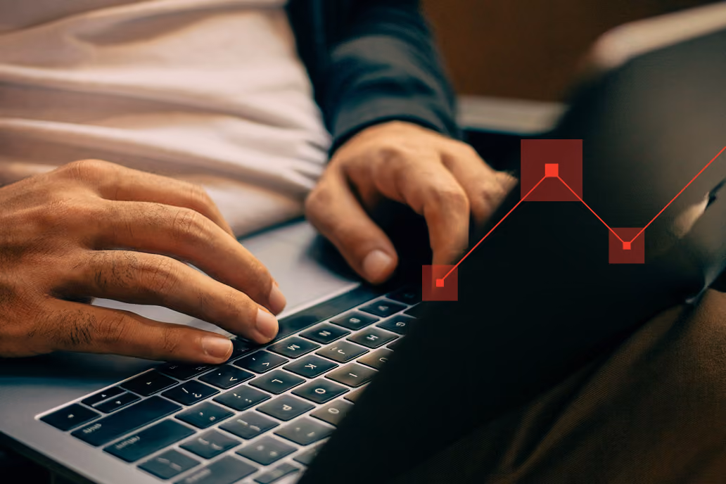 Close-up of hands typing on a laptop keyboard with a transparent red line graph overlay on the right side showing data points.