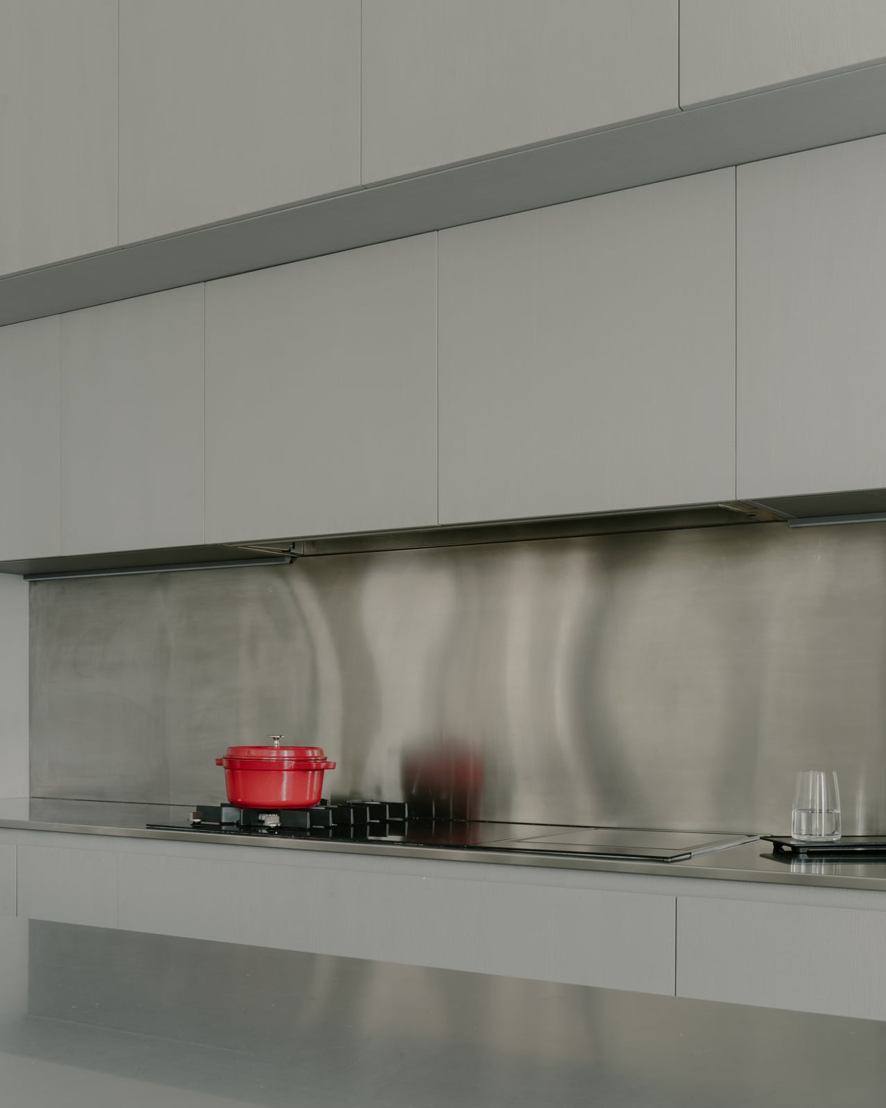Stainless steel splashback with a red pot on the hob along a long pale cabinet