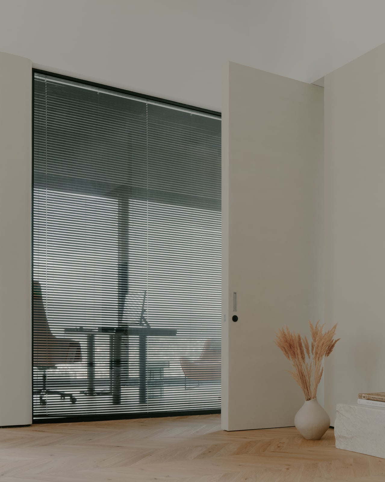 Glazed study behind blinds, with dried grasses in a tall vase