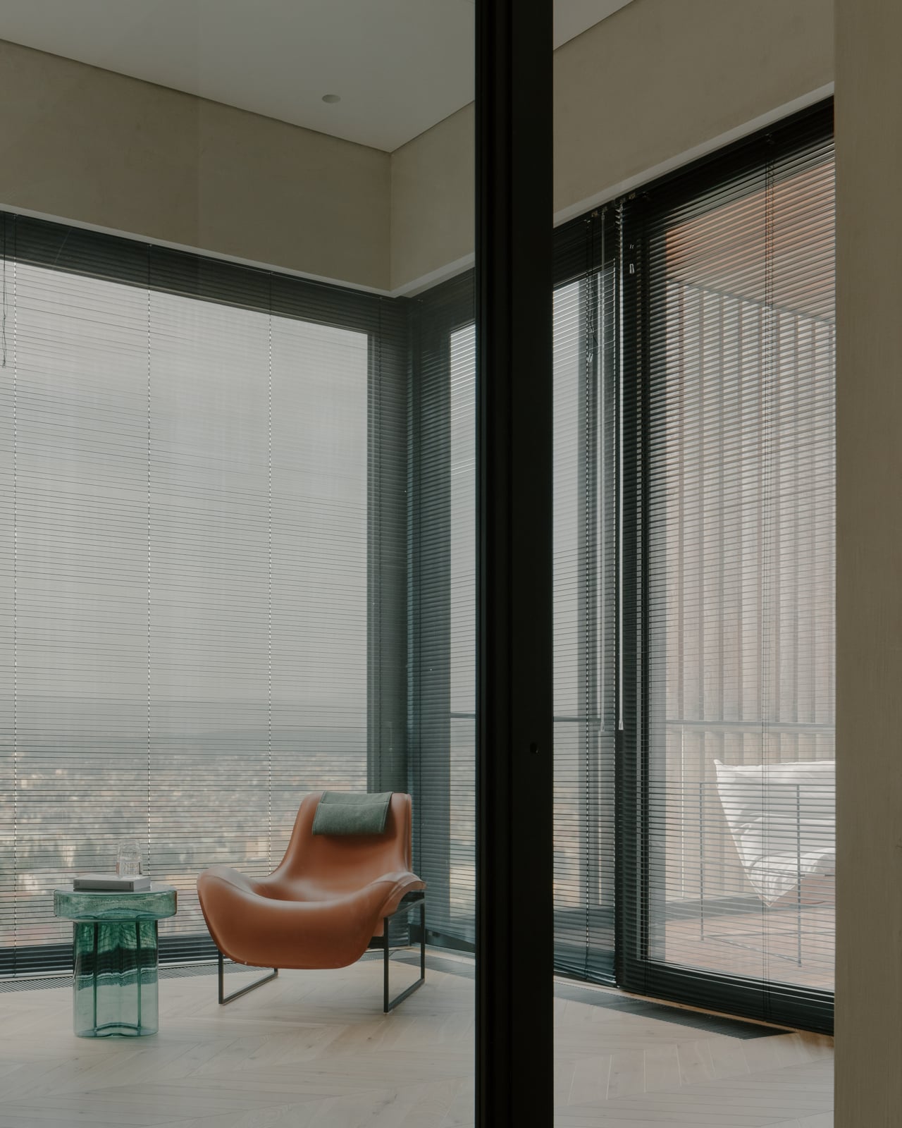 Corner window wall with a leather lounge chair and a green glass side table