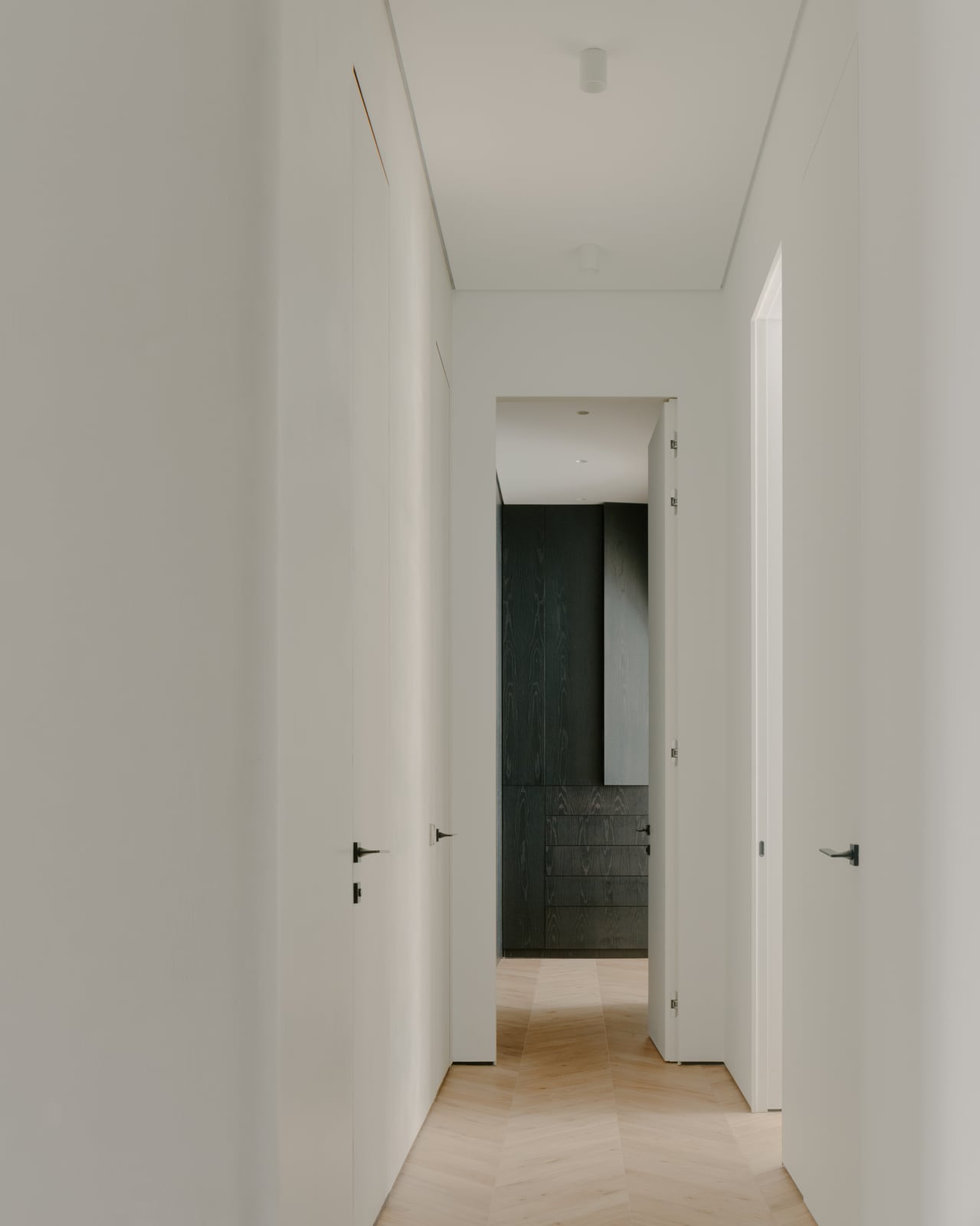 Narrow white corridor with a herringbone floor leading to a dark timber wardrobe