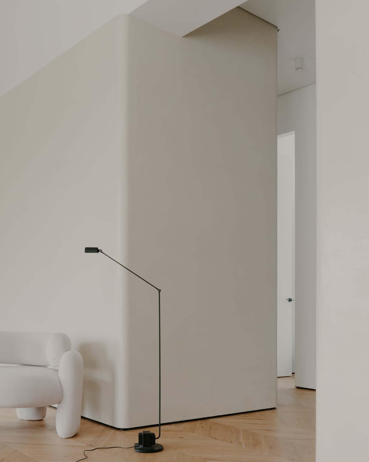 White wall with an arched recess, a floor lamp and a pale armchair