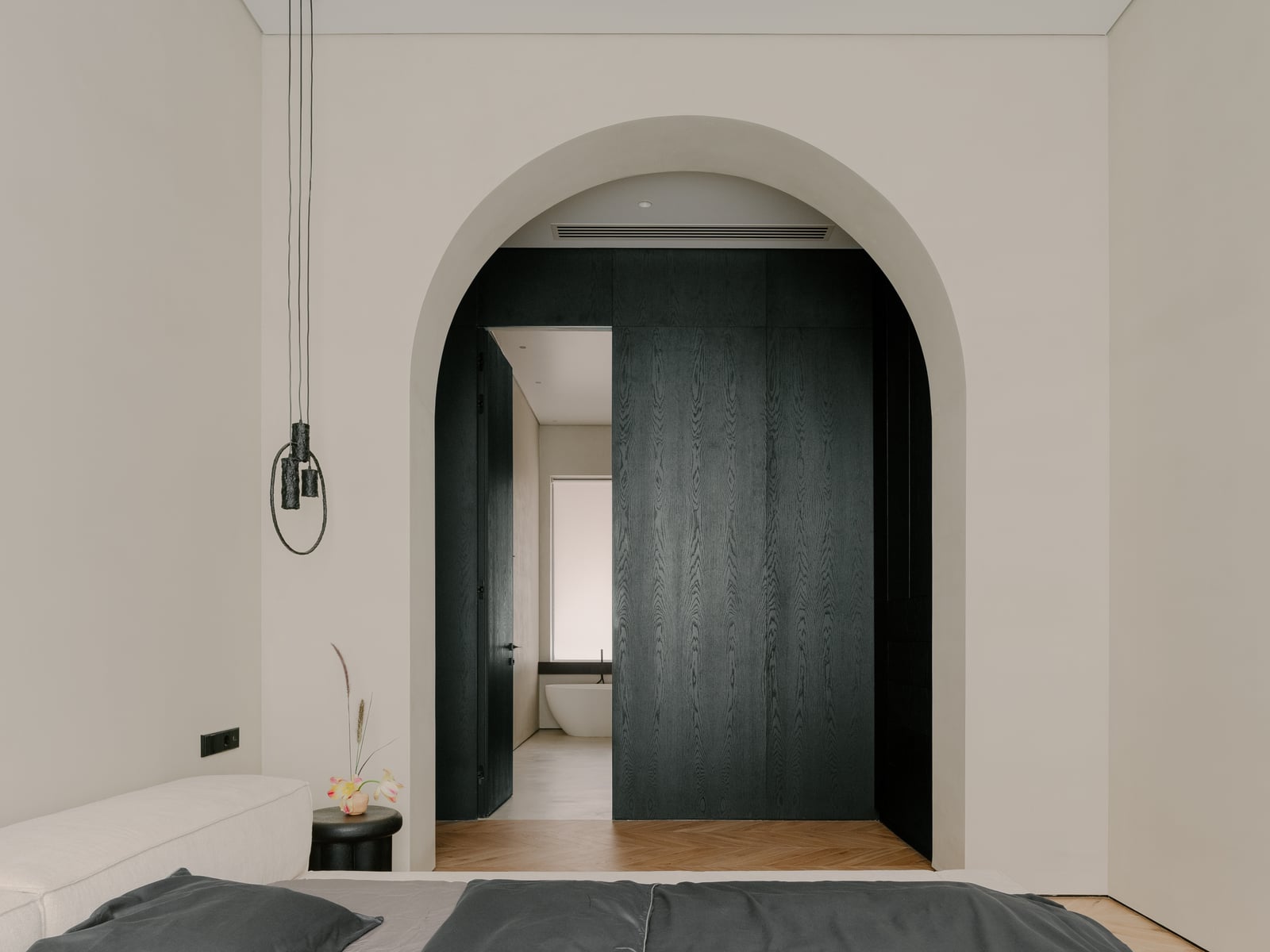 Bedroom with an arched dark doorway and a pendant light above the bed