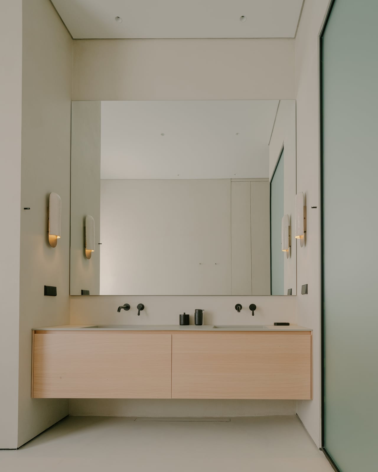 Bathroom with a mirror, twin basins on a light wooden vanity and a glass screen