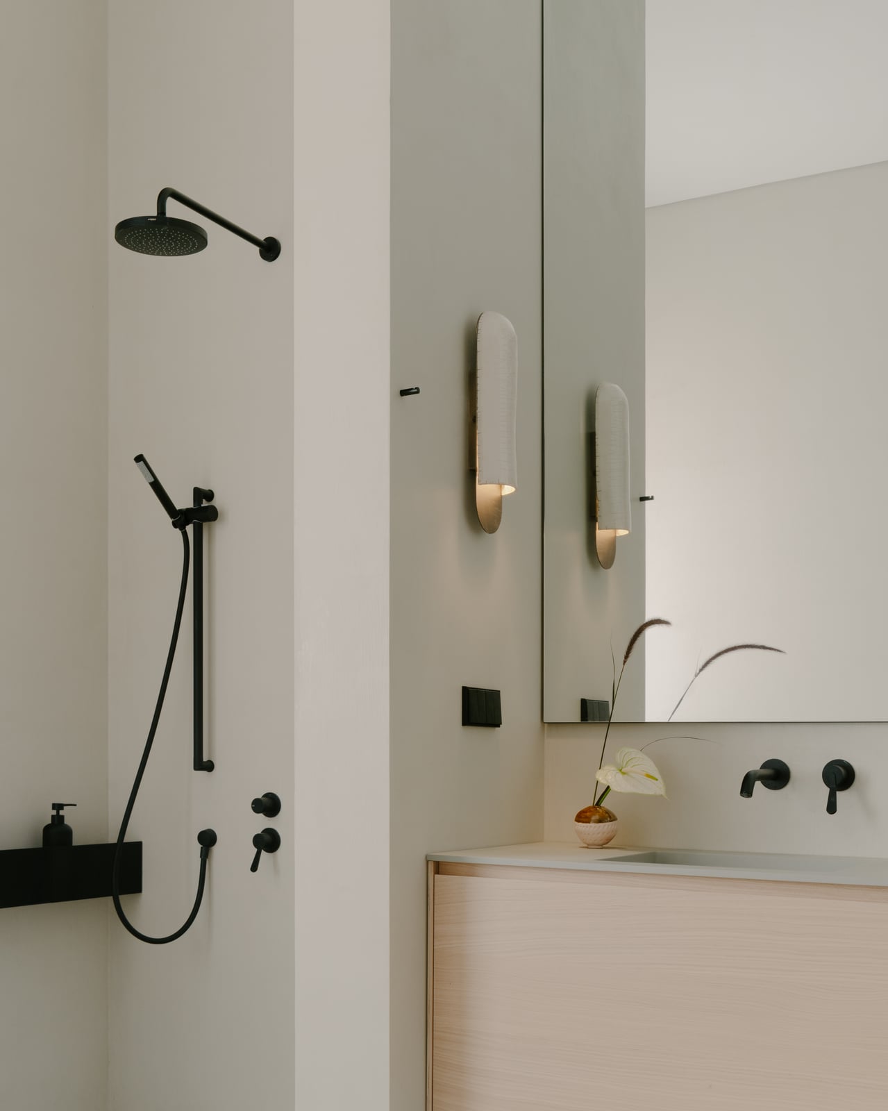 Shower with black fixtures and brass wall lights beside a basin