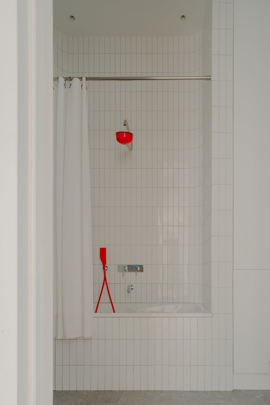 White tiled shower with a red fitting and a curtain rail