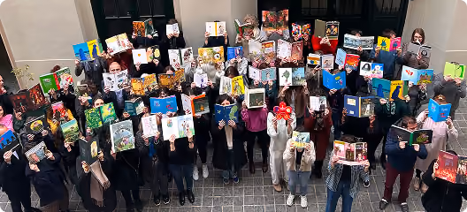 Un groupe de personnes debout en rangées dans une cour, tenant des livres ouverts devant leur visage, cachant leur identité.