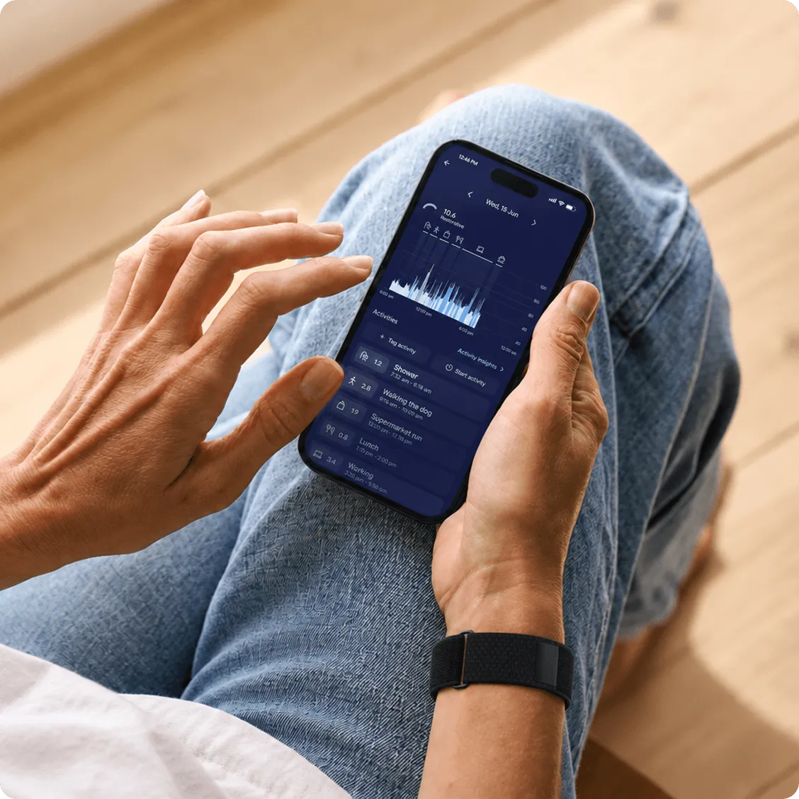 A person sitting in a chair, looking at the Visible app’s heart rate screen, with a chart of heart rate across the day and tagged activities.