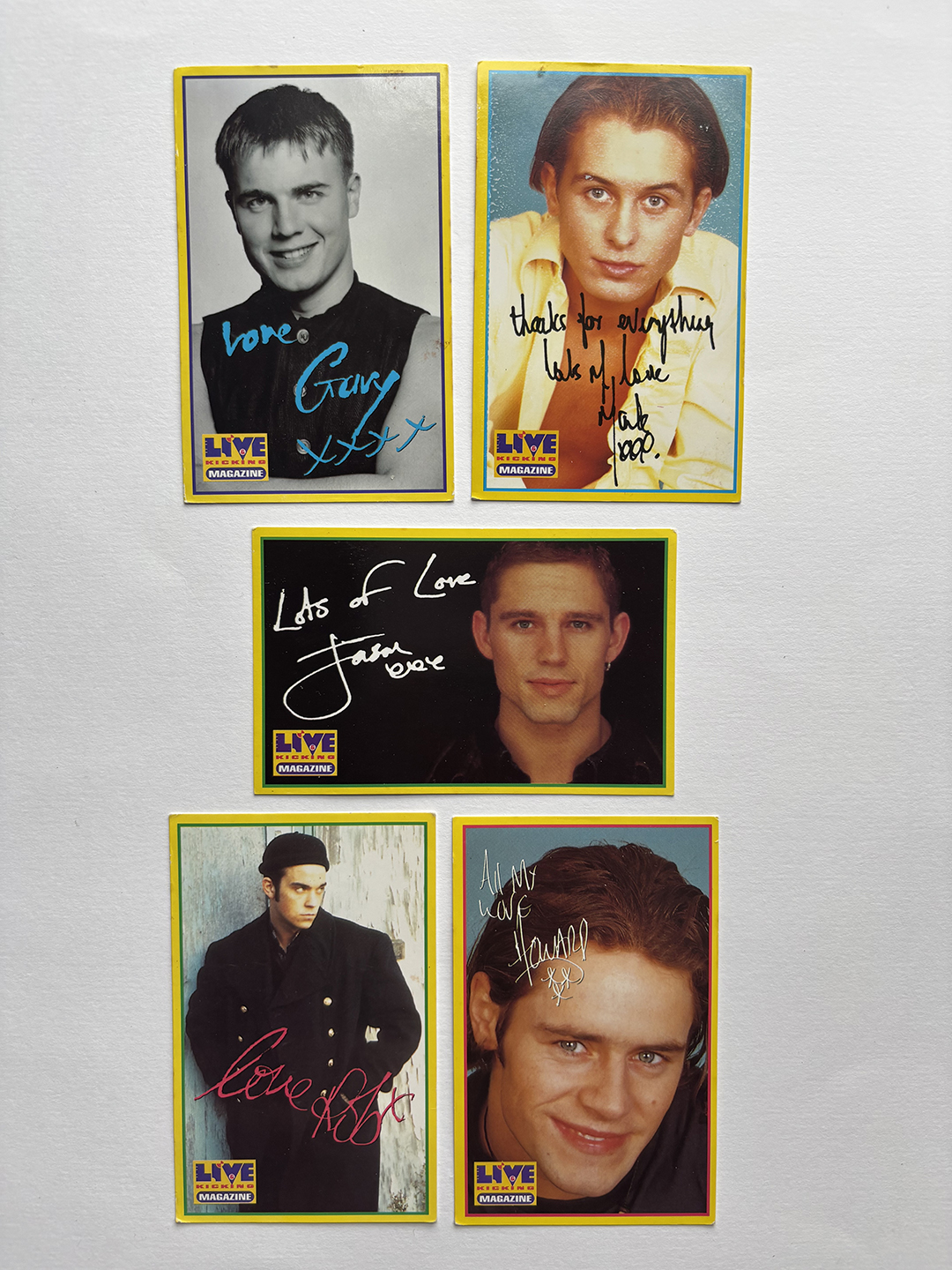 Five autographed magazine cards featuring members of the band Take That. Each card has a portrait photo and a personal signature message in colored ink. The cards include portraits of Gary, Mark, Jason, Robbie, and Howard with text messages like 'love Gary' and 'Lots of Love Jason'. Each card has a yellow border and the Live Magazine logo at the bottom left corner.