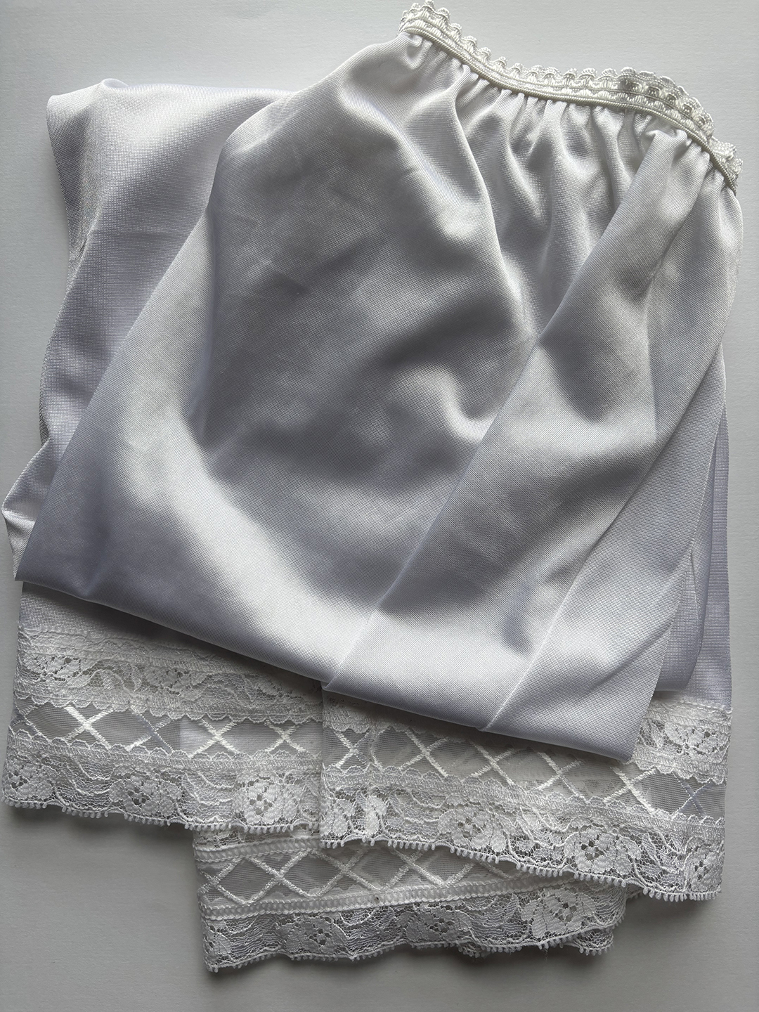 White petticoat fabric with a gathered waistband and decorative lace trim featuring floral and crisscross patterns.