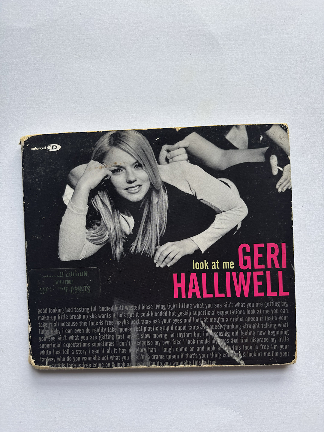 Worn CD cover for Geri Halliwell's 'Look At Me' single featuring a black-and-white photo of Geri Halliwell lying on her side, resting her head on her hand, smiling at the camera with text in bright pink and yellow.