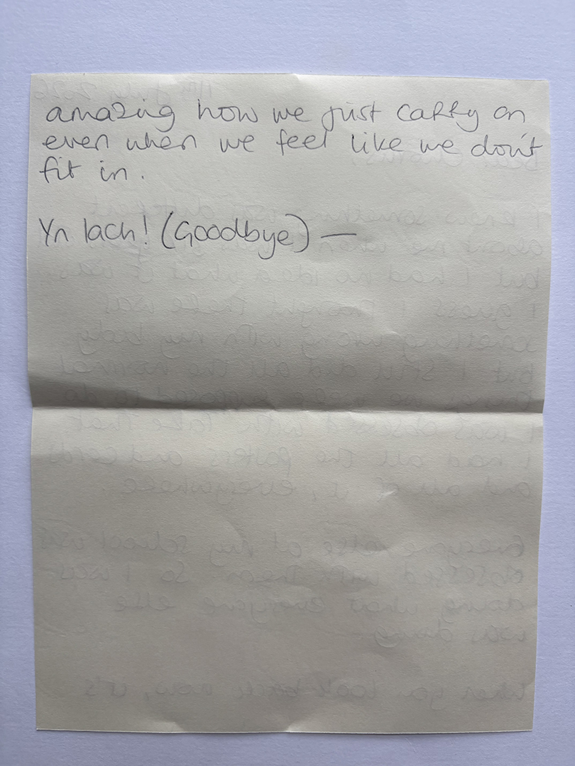 Handwritten note on cream paper saying: 'Amazing how we just carry on even when we feel like we don't fit in. Yn tach! (Goodbye)'