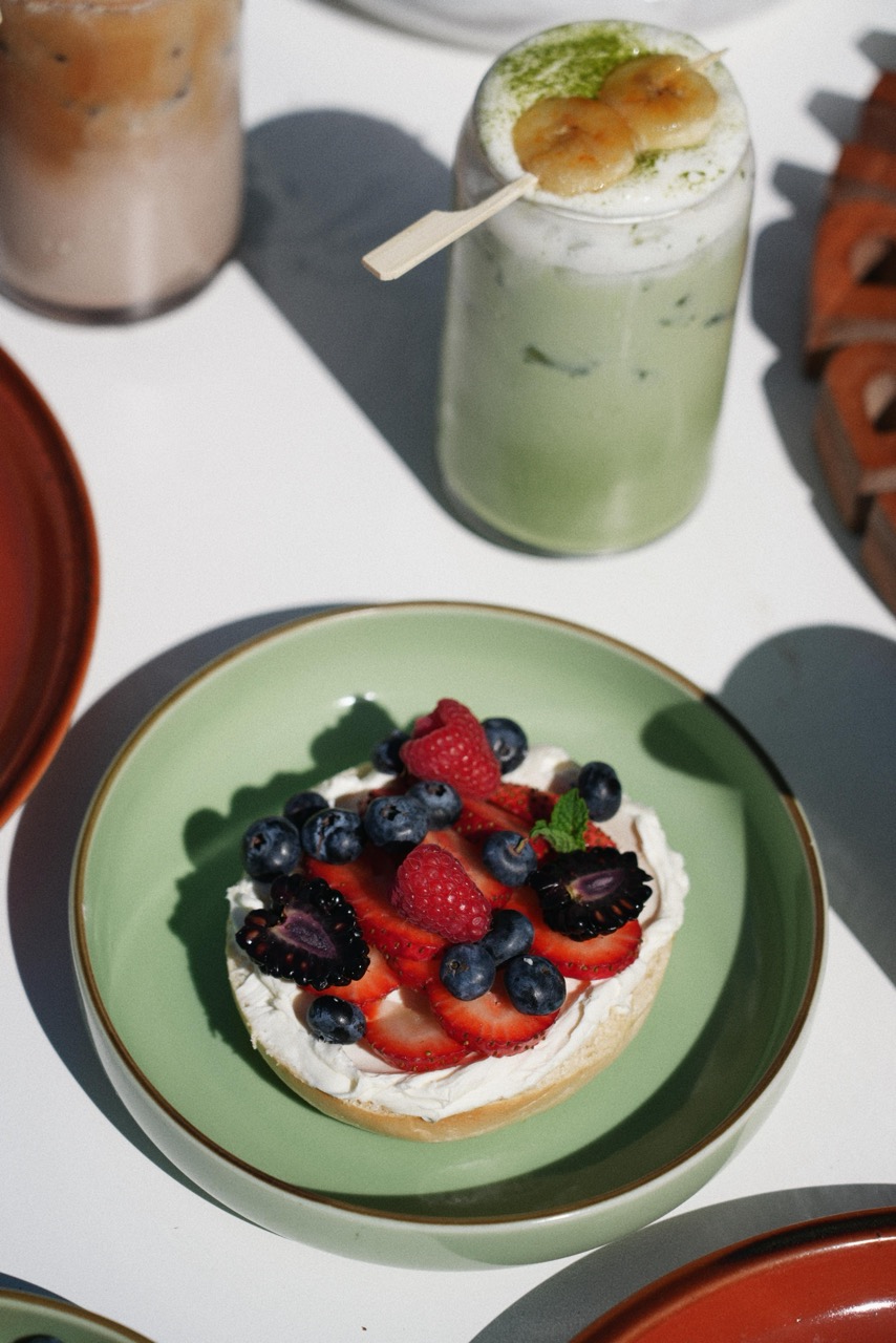 Small round tart on a green plate topped with cream, sliced strawberries, blueberries, raspberries, blackberries, and a small mint leaf.