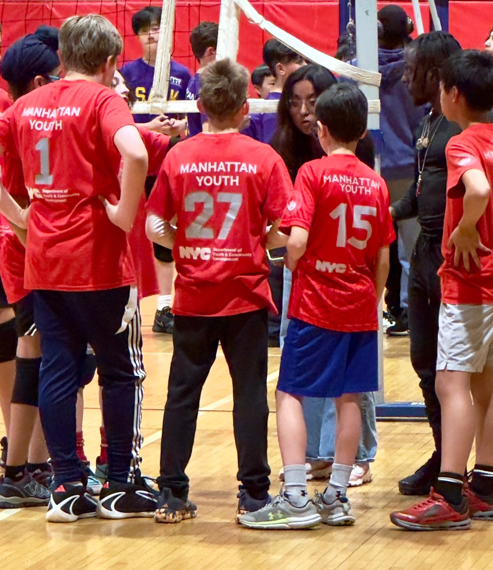 Anderson middle schoolers in red Manhattan Youth jerseys huddling together at a volleyball match