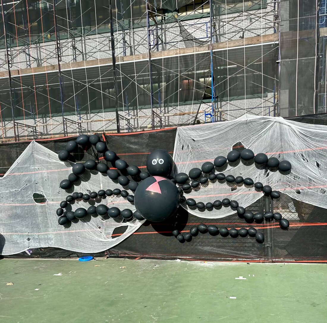A giant balloon spider on a web stretched across the schoolyard fence