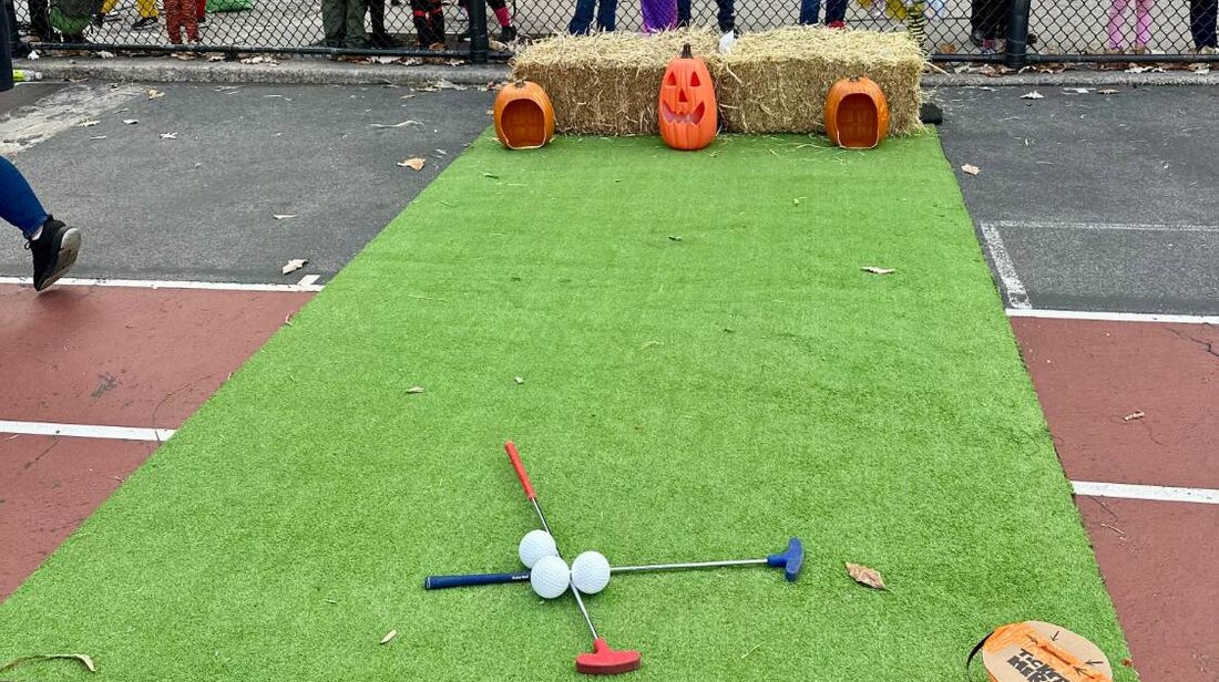 A mini golf lane on green turf with jack-o-lanterns at the far end