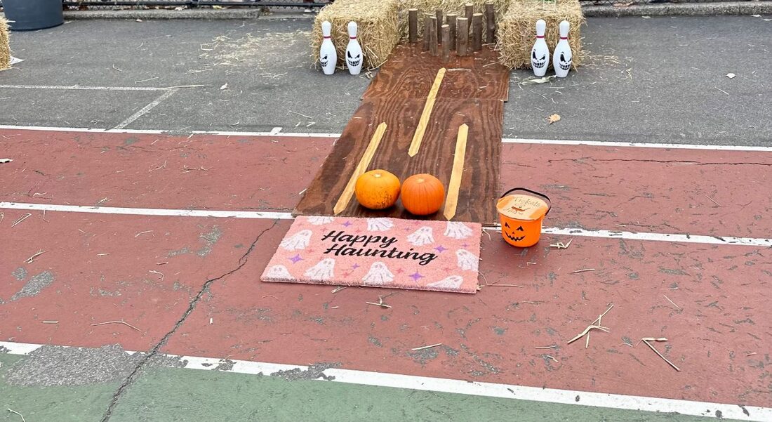 Pumpkin bowling: a wooden lane with ghost-painted pins and hay bales