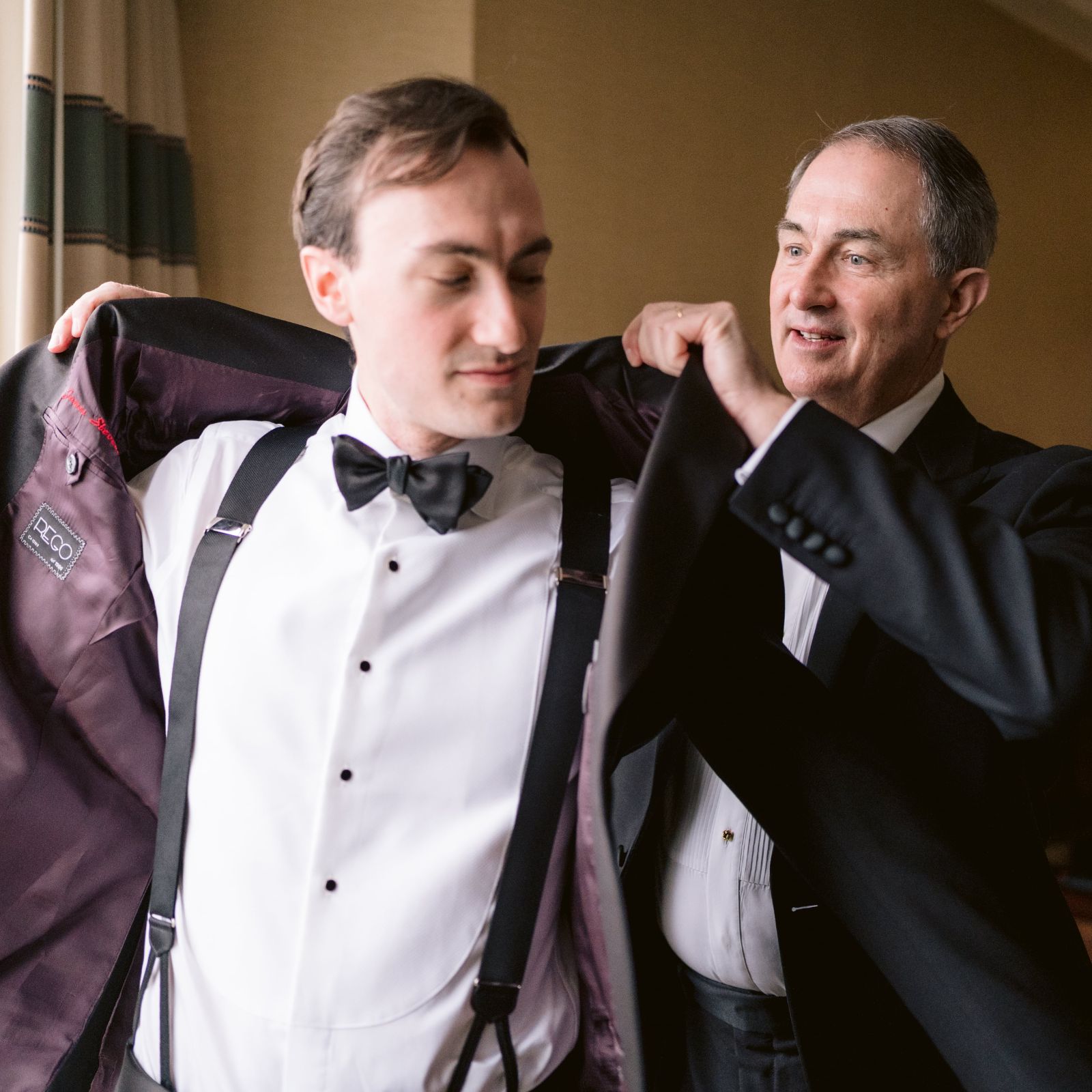 Groom putting on a tuxedo jacket with assistance before a wedding