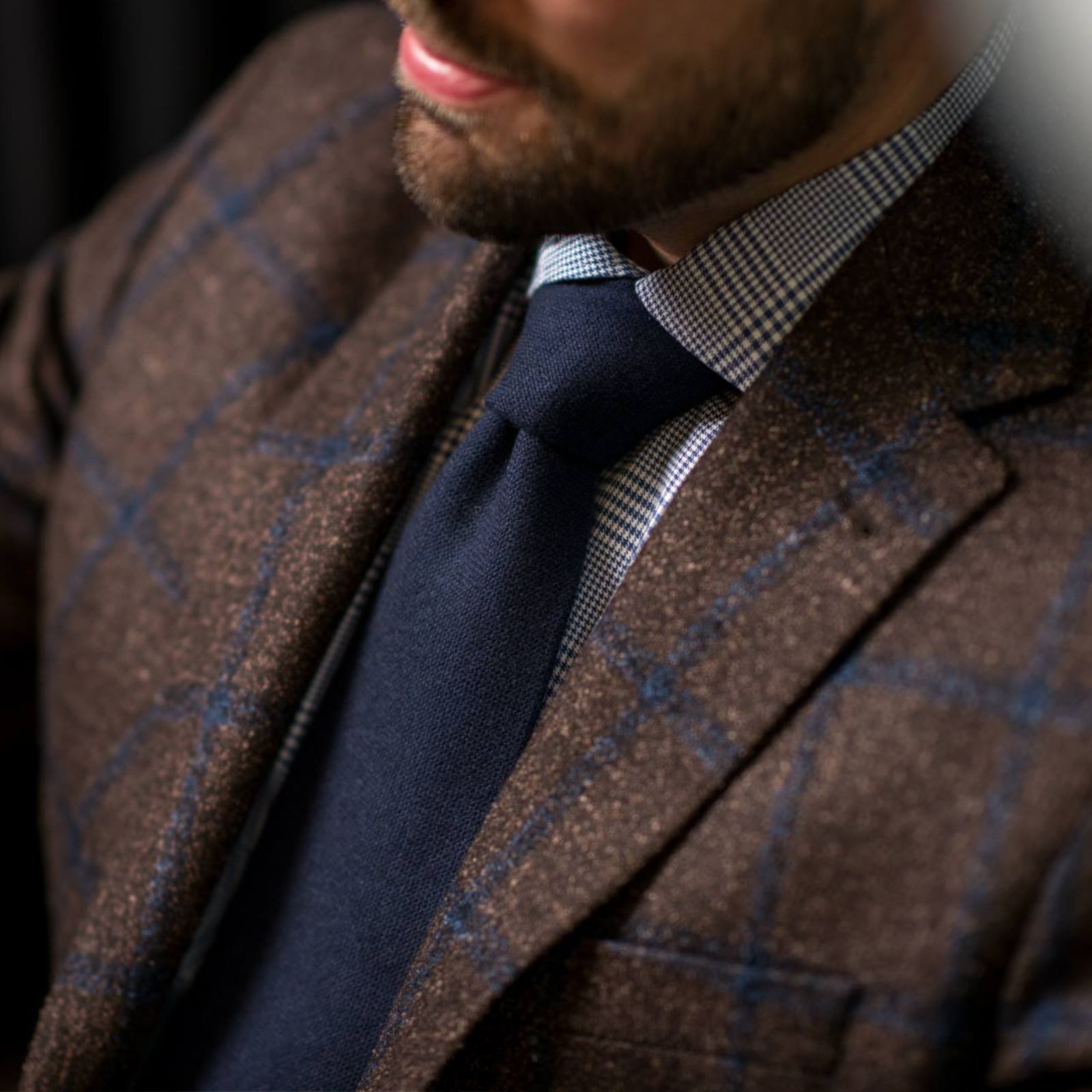 Close-up of a brown checked sport coat with navy tie and patterned shirt