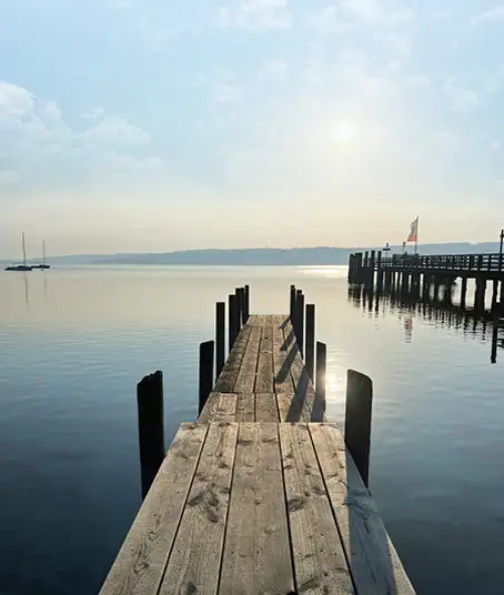 Ausblick auf einenweitläufigen blauen See mit einem Holzsteg vor dem Ufer