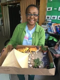 Teacher smiling and holding a student diorama project