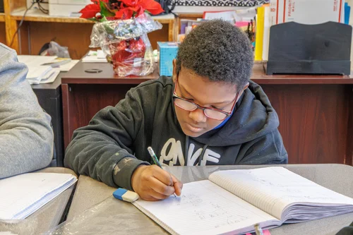 Student writing in a notebook at a classroom desk
